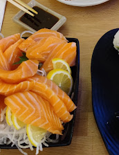 Black tray of orange salmon sashimi with lemon wedges and shredded daikon, beside chopsticks and blue dishes on a wooden table.