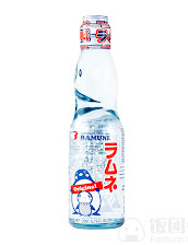 Clear glass Ramune soda bottle on a white background, with a blue-and-red Japanese label, red cap, and marble stopper; playful, nostalgic feel.