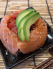 Close-up of a salmon sushi roll topped with avocado slices and salmon roe on a black plate, set on a bamboo mat; colorful and appetizing.