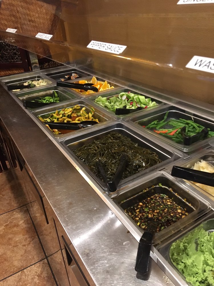 Self-serve salad bar with labeled trays of leafy greens, vegetables, seaweed, toppings, dressings, and bright guacamole in a clean display.