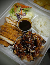 Takeout tray with white rice, salad, fried chicken strips, and saucy grilled meat, plus a small cup of dark dipping sauce; hearty meal.